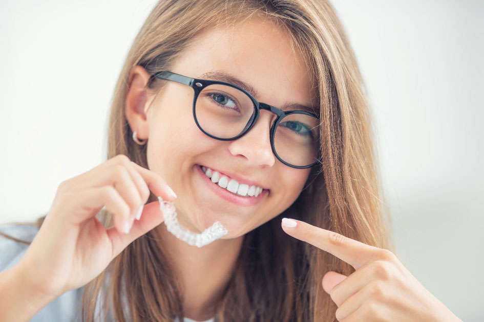 Une patiente adolescente montre son traitement orthodontique et sourit.